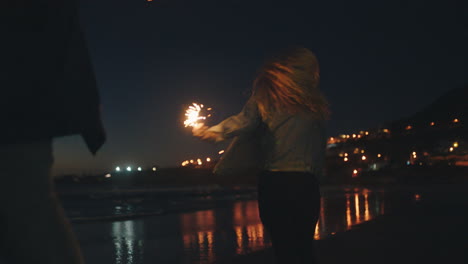 Amigas-Bailando-Con-Bengalas-En-La-Playa-Por-La-Noche-Celebrando-La-Víspera-De-Año-Nuevo-Divirtiéndose-Bailando-Con-Fuegos-Artificiales-De-Bengala-Junto-Al-Mar