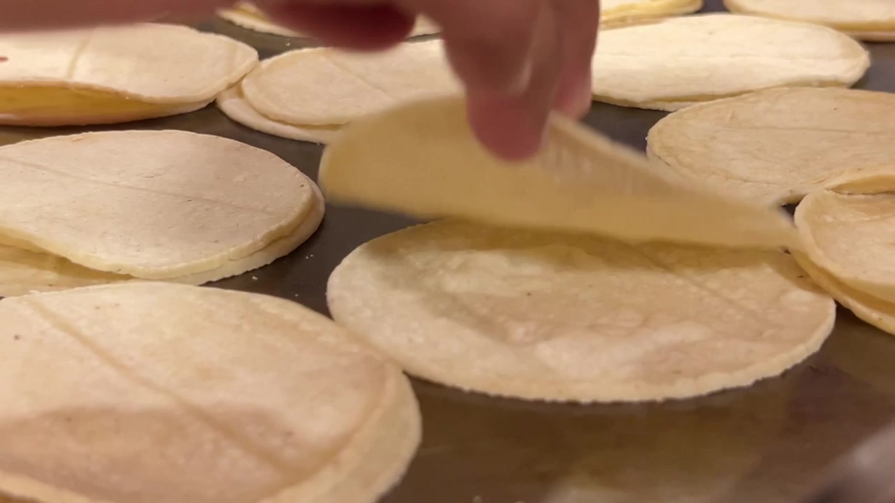 Corn tortillas on a flat griddle cooking, close-up shot, showcasing a golden and warm texture