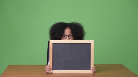 young cute african girl with afro hair showing blackboard while sitting