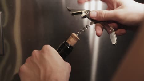 screwing a cork screw into a cork of a wine bottle infront of a fridge - close up