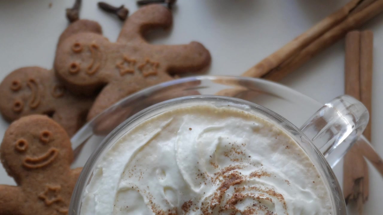 Biscotti di pan di zenzero festivi e una bevanda cremosa guarnita con panna montata e cannella, ripresi dall'alto.