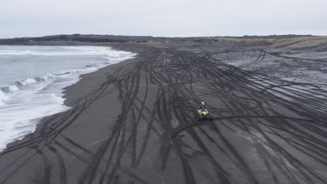 aerial of quad bike riding on black sand beach in volcanic iceland