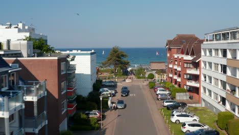 Vista-Aérea-Volando-Entre-La-Calle-Del-Edificio-Frente-Al-Agua-De-Mar-Azul-Claro-Báltico-En-Scharbeutz,-Alemania,-Dolly-In,-Día