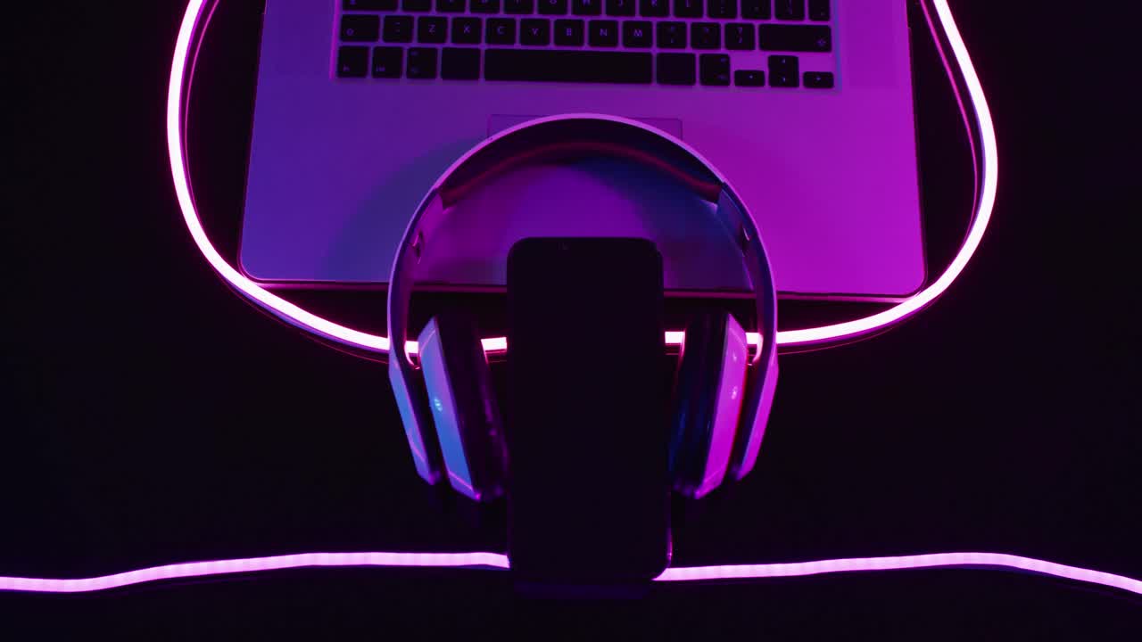 composición de computadora portátil, auriculares y teléfono inteligente con luces de neón rosadas sobre fondo negro
