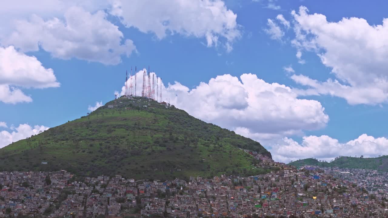 Green hill with antennas towering over a city on the hillside under a blue sky