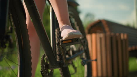 close-up of cyclist s leg in pink sneakers gently tapping on bicycle pedal, preparing for ride, sunlight illuminates scene with blurred background featuring park greenery