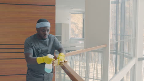 cleaning man wearing gloves cleaning stair railing inside an office building 1