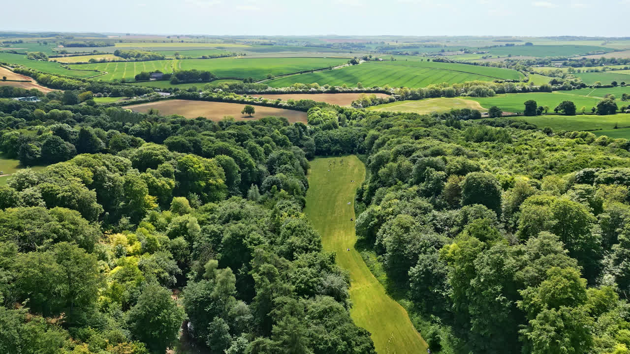 Aerial drone video of a UK summer park&mdash;individuals savoring a meandering stream, delightful picnic spots, and a wooded attraction