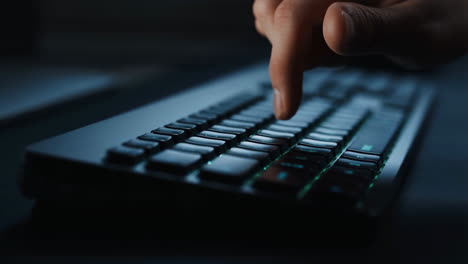 close-up of a hand typing on a backlit keyboard in a dimly lit room