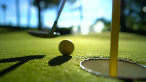 mini golf yellow ball with a bat near the hole at sunset