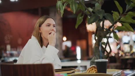 close-up of lady enjoying fries with a warm smile in a casual dining mall setting, she appears content while eating, with a soft background of colorful mall lights