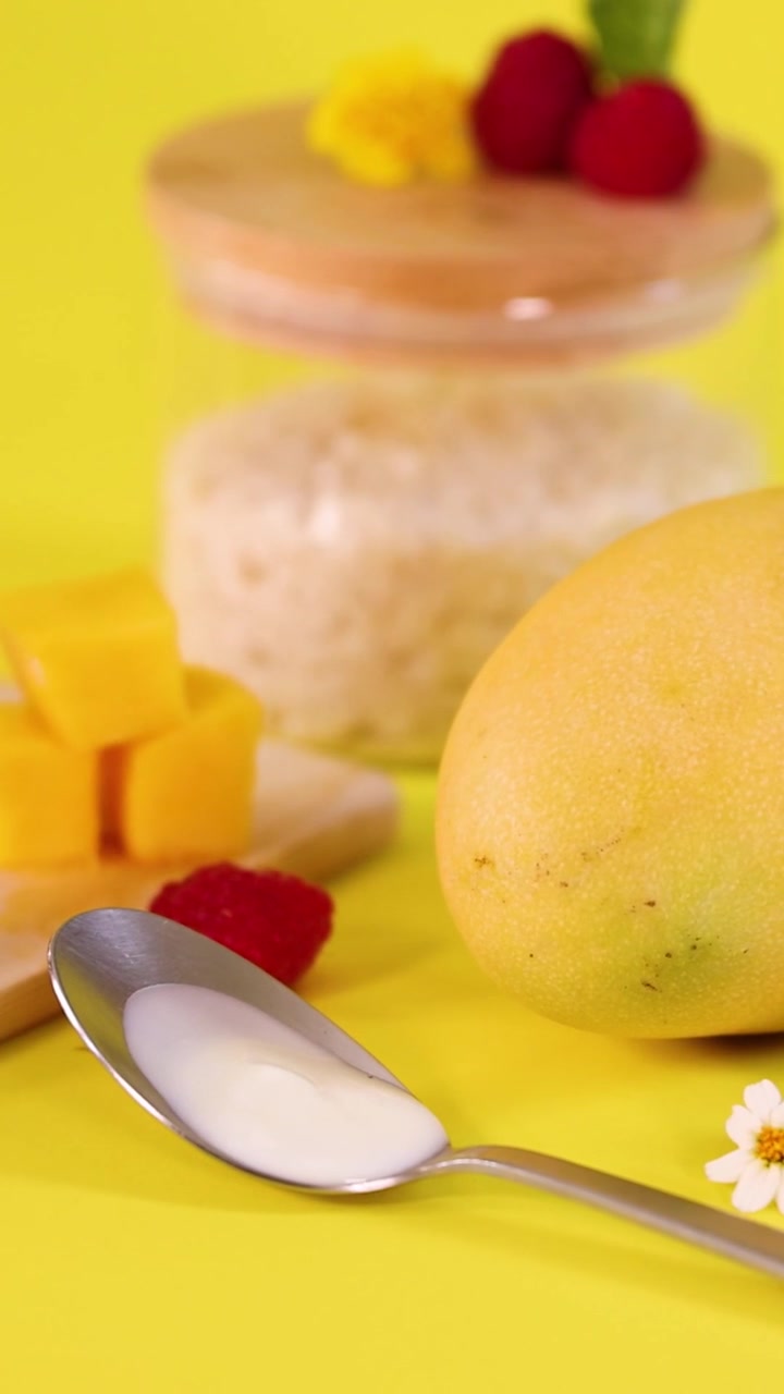 Un'inquadratura verticale vibrante che mostra mango fresco, lamponi e fiori commestibili su una superficie gialla