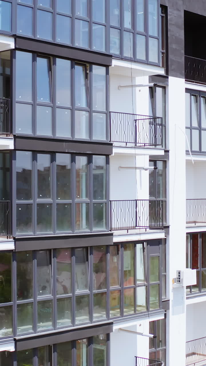 Beautiful new housing apartments. Modern facade of a high-rise building with a cityscape reflection in windows. Multi-storey building in white and black colors. Front view. Vertical video