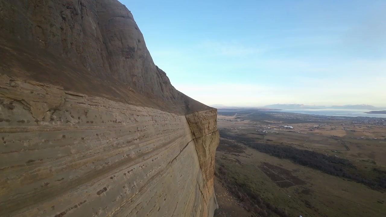 Falesia di arenaria a picco del Cerro Dorotea che si erge sopra una vasta valle aperta, con il fiordo distante vicino a Puerto Natales, Cile, visibile sotto, ripresa aerea FPV.