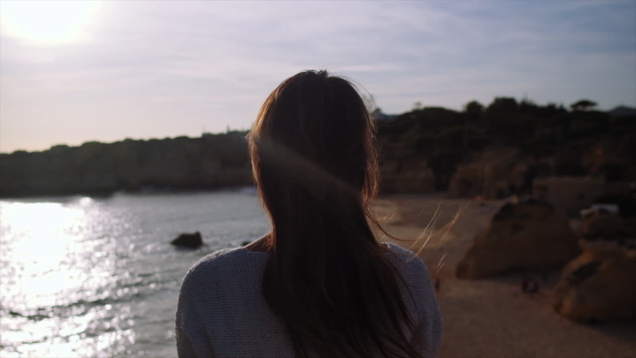 cerrar la vista trasera de la niña levantando los brazos en el aire durante un hermoso día soleado y el paisaje oceánico en el fondo