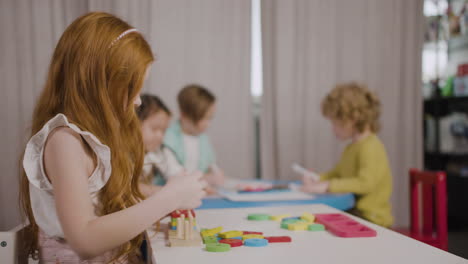 ginger little girl in a montessori school playing with shapes stacking while her classmates drawing