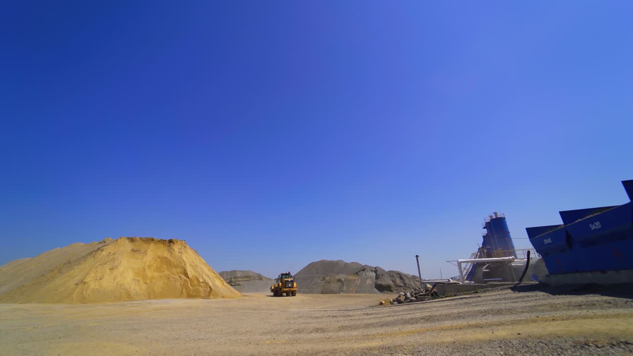 Asphalt manufacturing plant outdoors. Excavator working . Piles of sand on the environmental background.