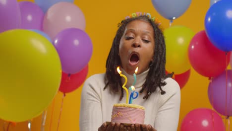 Studio-Portrait-Of-Woman-Wearing-Birthday-Headband-Celebrating-Birthday-Blowing-Out-Candles-On-Cake-2