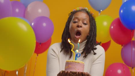 retrato de estudio de una mujer con una cinta para la cabeza de cumpleaños celebrando su cumpleaños soplando velas en el pastel 2