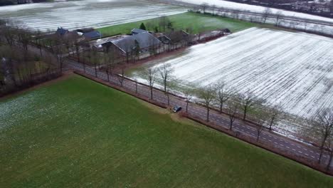 Aerial-view-above-agricultural-fields-covered-in-snow-and-farm-buildings,-winter-landscape-in-the-Netherlands