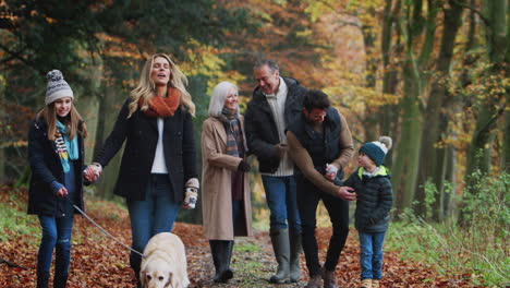 smiling multi-generation family with dog walking along path through autumn countryside together