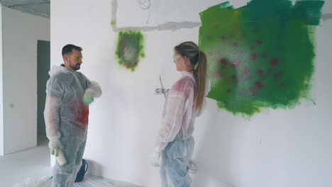 joyful girl paints boyfriend in protective suit near wall