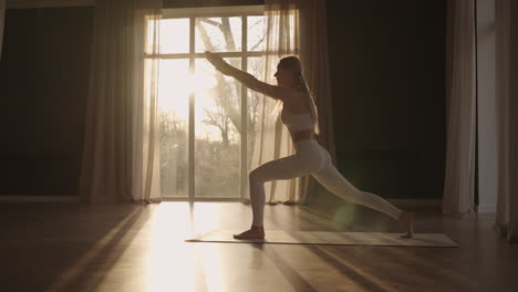 Lens-flare-:A-young-woman-in-white-sportswear-is-stretching-with-a-large-hall-with-large-windows-in-a-slow-motion-scheme-the-sun's-rays-shine-through-the-window.-Healthy-lifestyle-healthy-morning