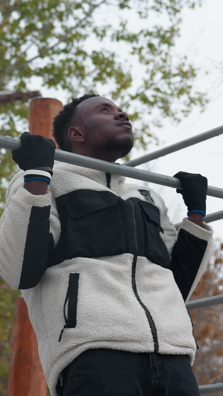 niño realizando ejercicios de tracción en una barra de entrenamiento al aire libre en invierno. vestido con una cálida chaqueta de lana y guantes, agarra la barra con determinación, suelo cubierto de nieve, árboles sin hojas y fondo urbano