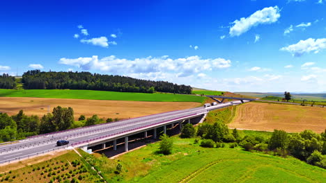 scenic highway stretches on. a long highway winds through lush green fields and forests under a bright blue sky with scattered clouds