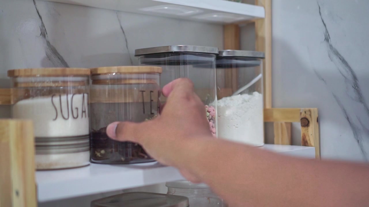 hand placing tea jar into kitchen counter, glass storage container, home cooking footage scene.
