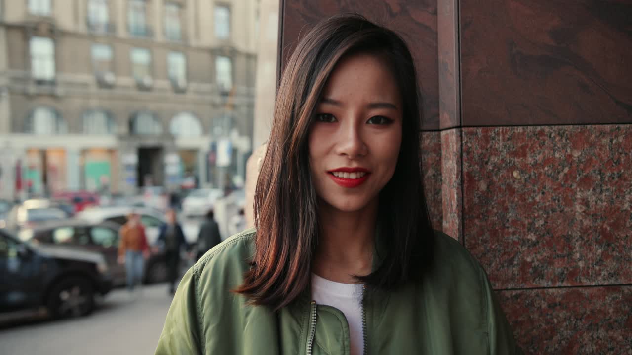 Portrait Shot Of The Pretty Young Woman Standing At The Wall In The Center City And Smiling To The Camera On The Summer Day