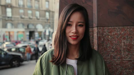 portrait shot of the pretty young woman standing at the wall in the center city and smiling to the camera on the summer day