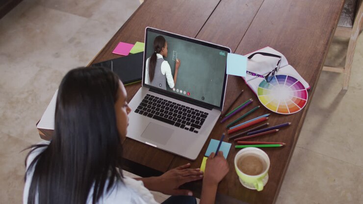 Studentessa caucasica che utilizza un laptop in videochiamata con un'insegnante donna, prendendo appunti.