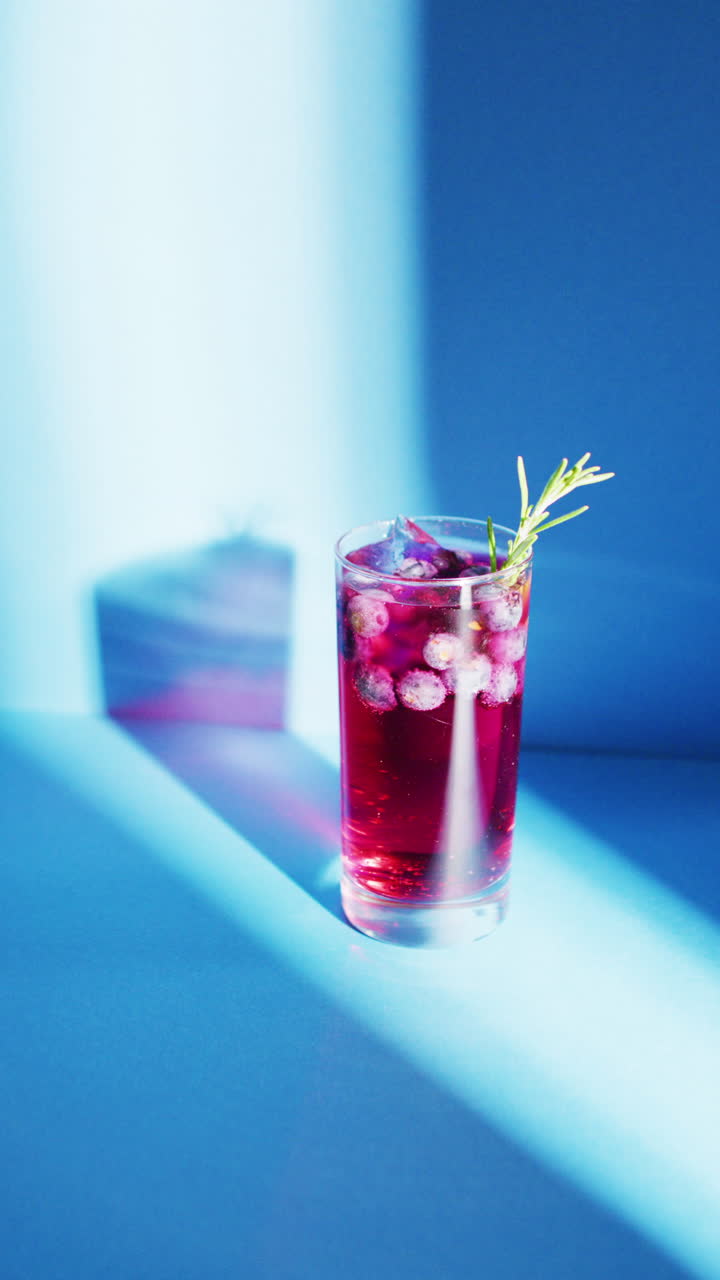 Vertical video of close up of drink with blueberries on blue background