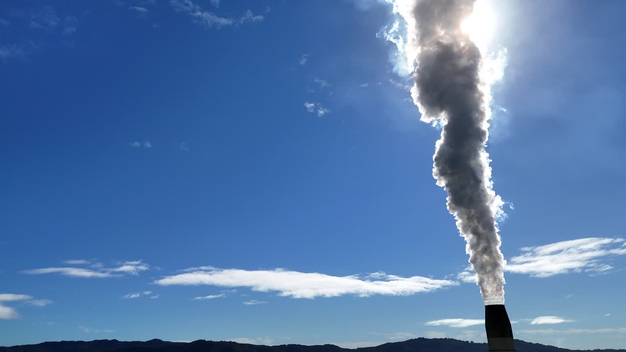 A smokestack releases thick smoke into a clear blue sky, highlighting environmental pollution under bright daylight