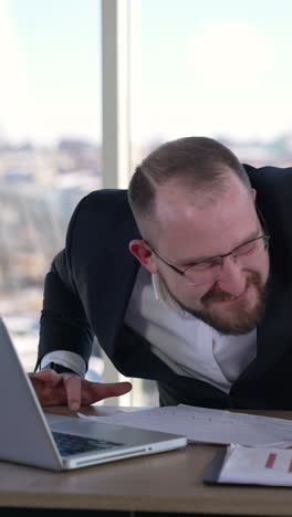 man doing funny faces sitting in front of laptop. mad businessman typing nervously with fingers on keyboard and looking to the sides. entrepreneur with insane face in office. vertical video