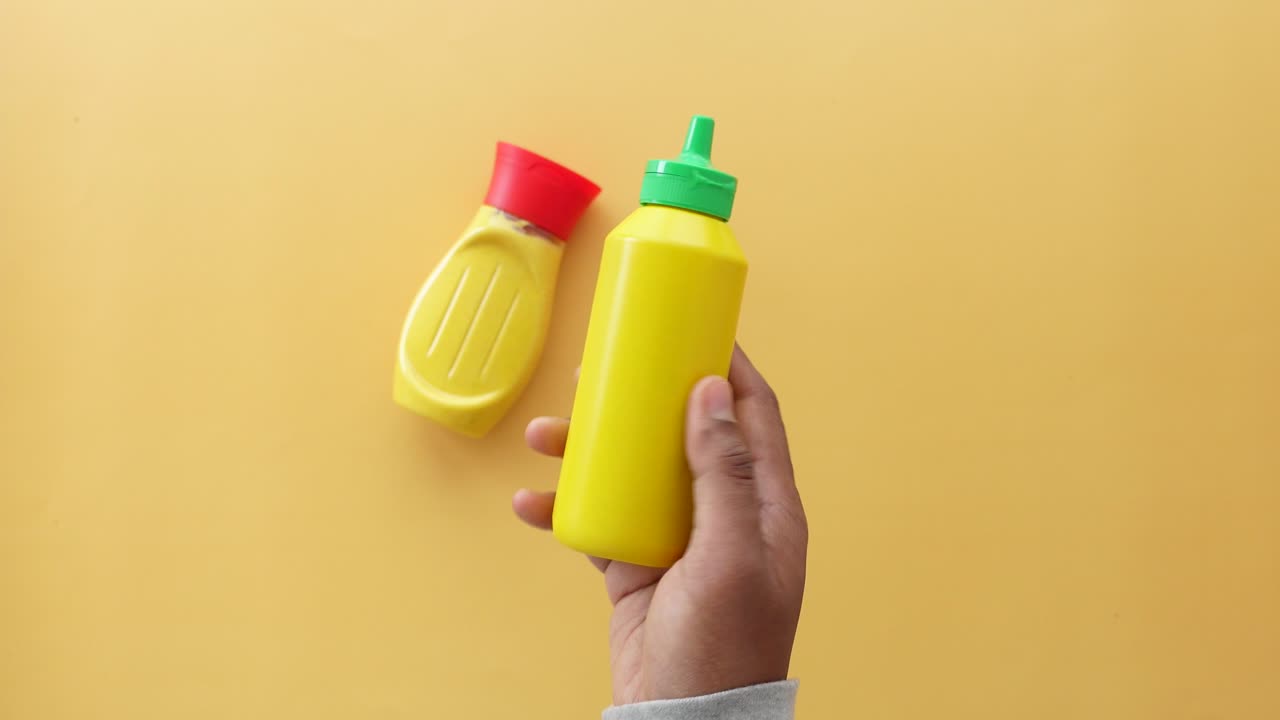 mano sosteniendo una botella de mostaza sobre un fondo amarillo