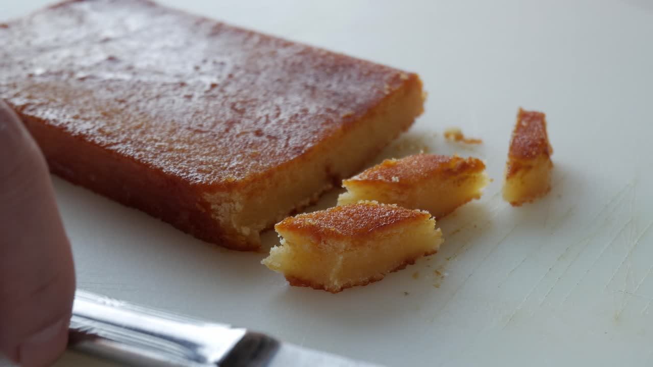 Sliced toasted egg yolk turron on a white cutting board with a knife