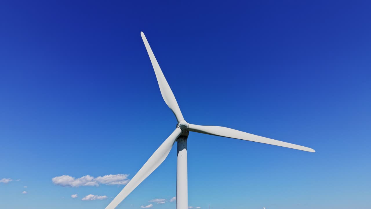 Una turbina eolica si staglia alta contro il cielo blu con nuvole bianche.