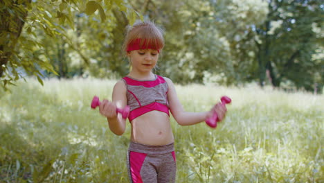 Athletic-young-sporty-fit-child-kid-girl-working-out-dumbbells-in-park-performing-bicep-exercising