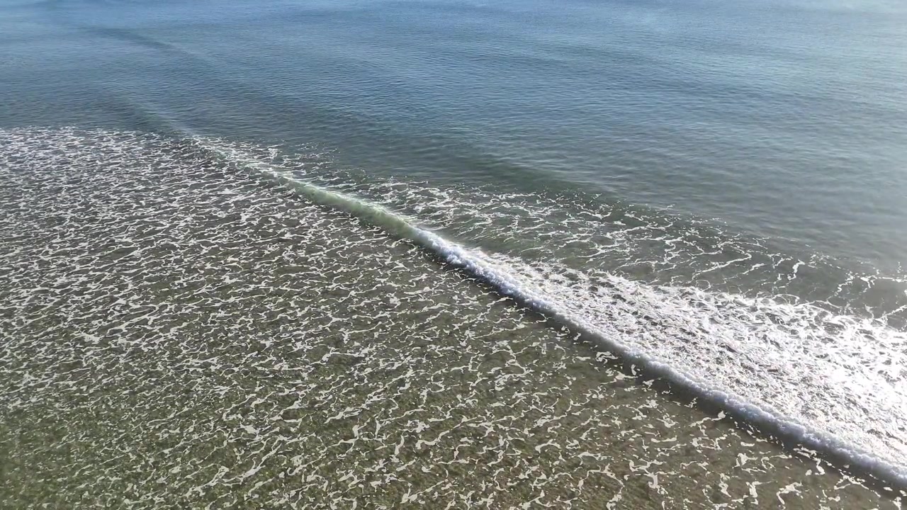 Vista aerea di dolci onde dell'oceano che si infrangono su una spiaggia sabbiosa