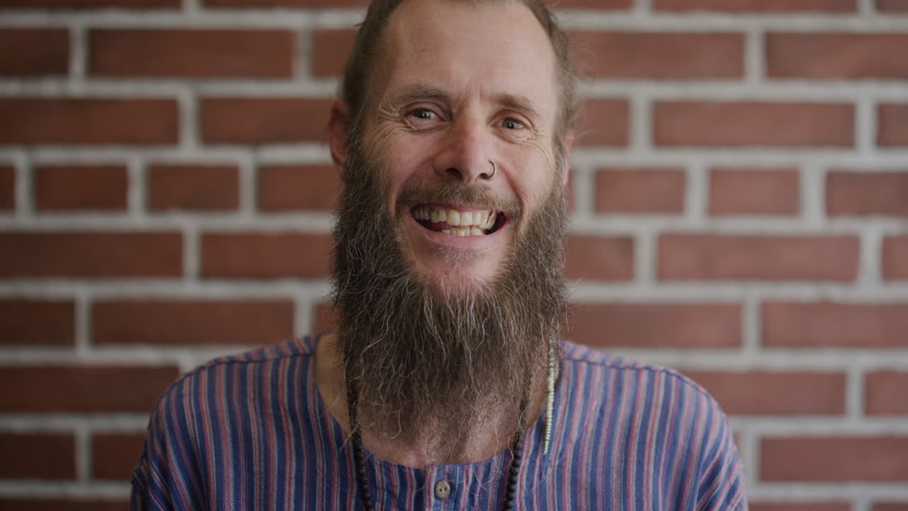 portrait mature bearded hippie man laughing happy enjoying relaxed carefree lifestyle eccentric caucasian male wearing nose ring on brick wall background
