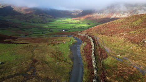 Mountain-pass-with-green-valley-beyond-surrounded-by-cloud-shrouded-mountains-lit-by-early-morning-autumn-sunlight