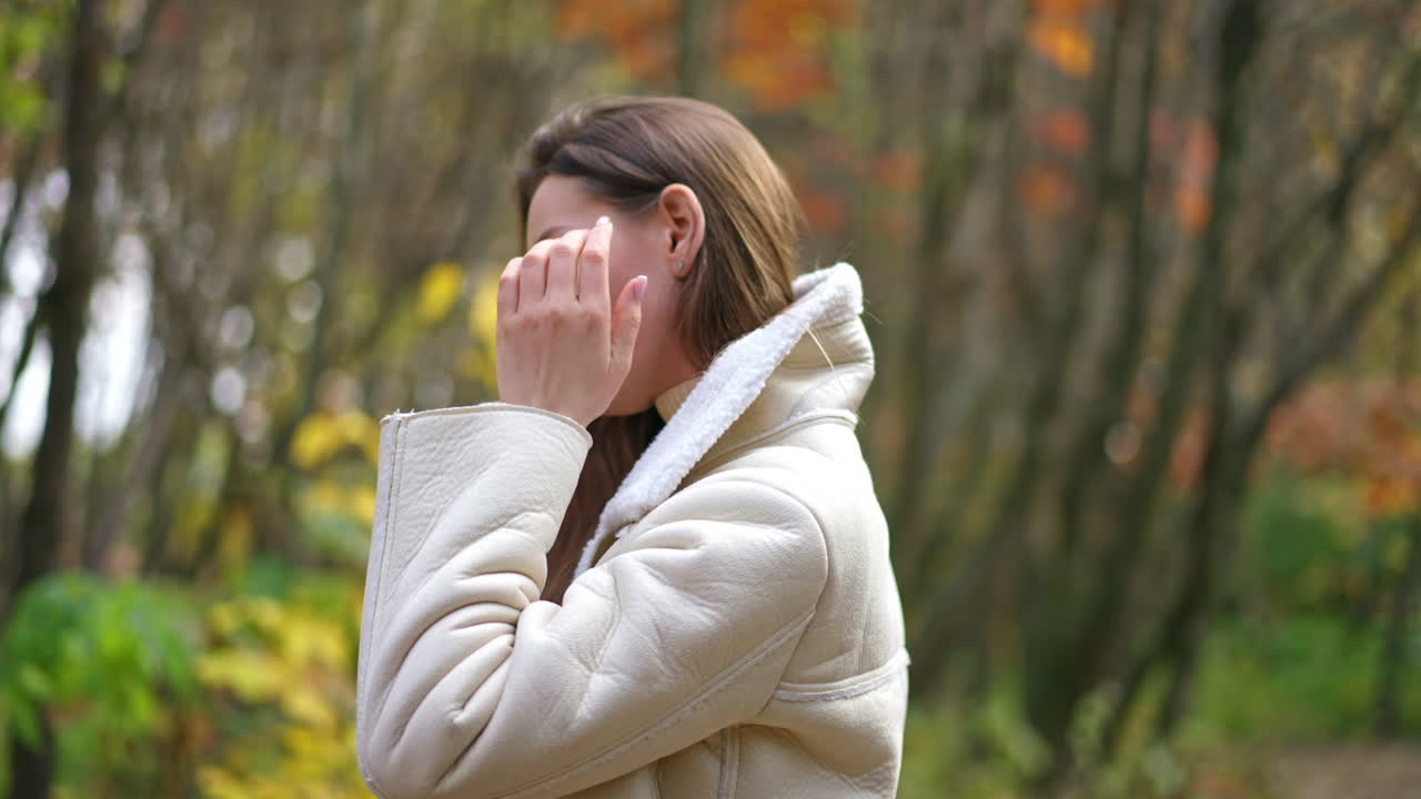 Relaxed calm woman wearing warm jacket touching long hair. Smiling lady at the walk along the autumn colorful park.