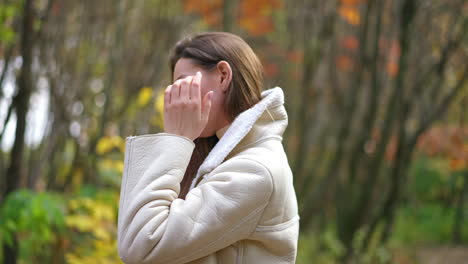 relaxed calm woman wearing warm jacket touching long hair. smiling lady at the walk along the autumn colorful park.