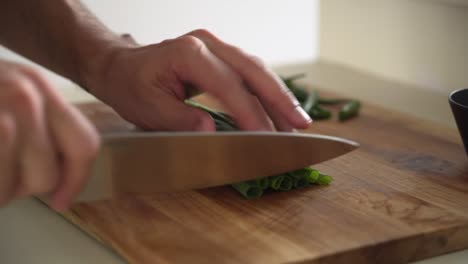 chef profesional cortando cebolletas en una tabla de cortar de madera, plano medio