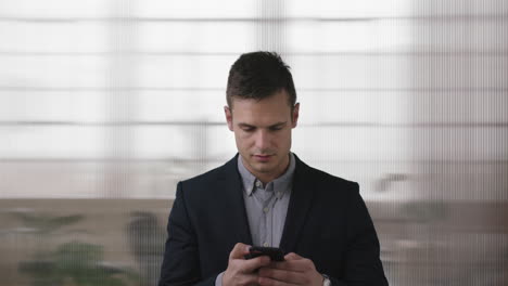 Retrato-De-Un-Joven-Apuesto-Hombre-De-Negocios-Exitoso-Comprobando-Reloj-De-Pulsera-Mensajes-De-Texto-Navegando-Usando-Un-Teléfono-Inteligente-En-El-Fondo-Del-Espacio-De-Trabajo-De-Oficina