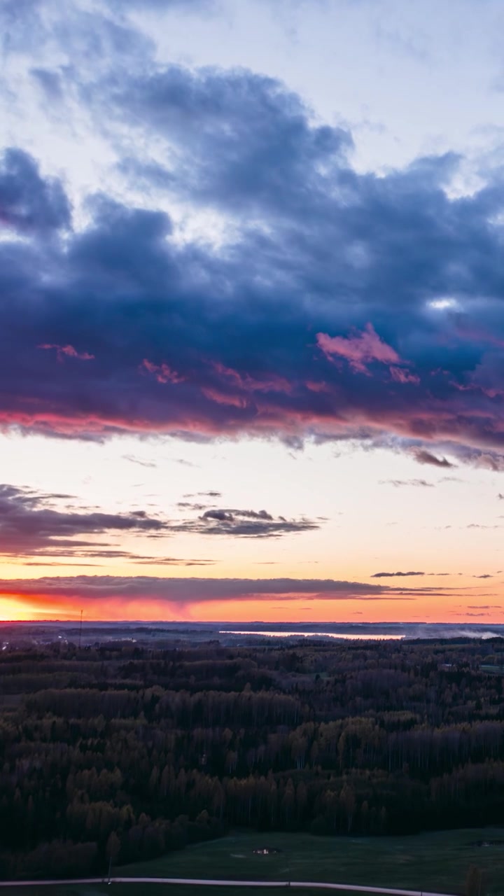 Vertical aerial drone hyperlapse of a vibrant sunset over vast forests and green fields under dramatic clouds. Colorful evening over countryside landscape.