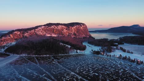 la antena retrocede y se eleva lejos de la cima de una montaña frente a un acantilado durante un amanecer de invierno que revela el lago brumoso y los bosques interminables detrás