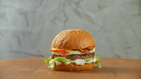 Gran-Hamburguesa-Con-Chuleta-De-Ternera,-Tomates,-Champiñones-Y-Pepinos-Con-Queso-Derretido-Gira-Sobre-Una-Tabla-De-Madera-Sobre-Un-Fondo-Claro.